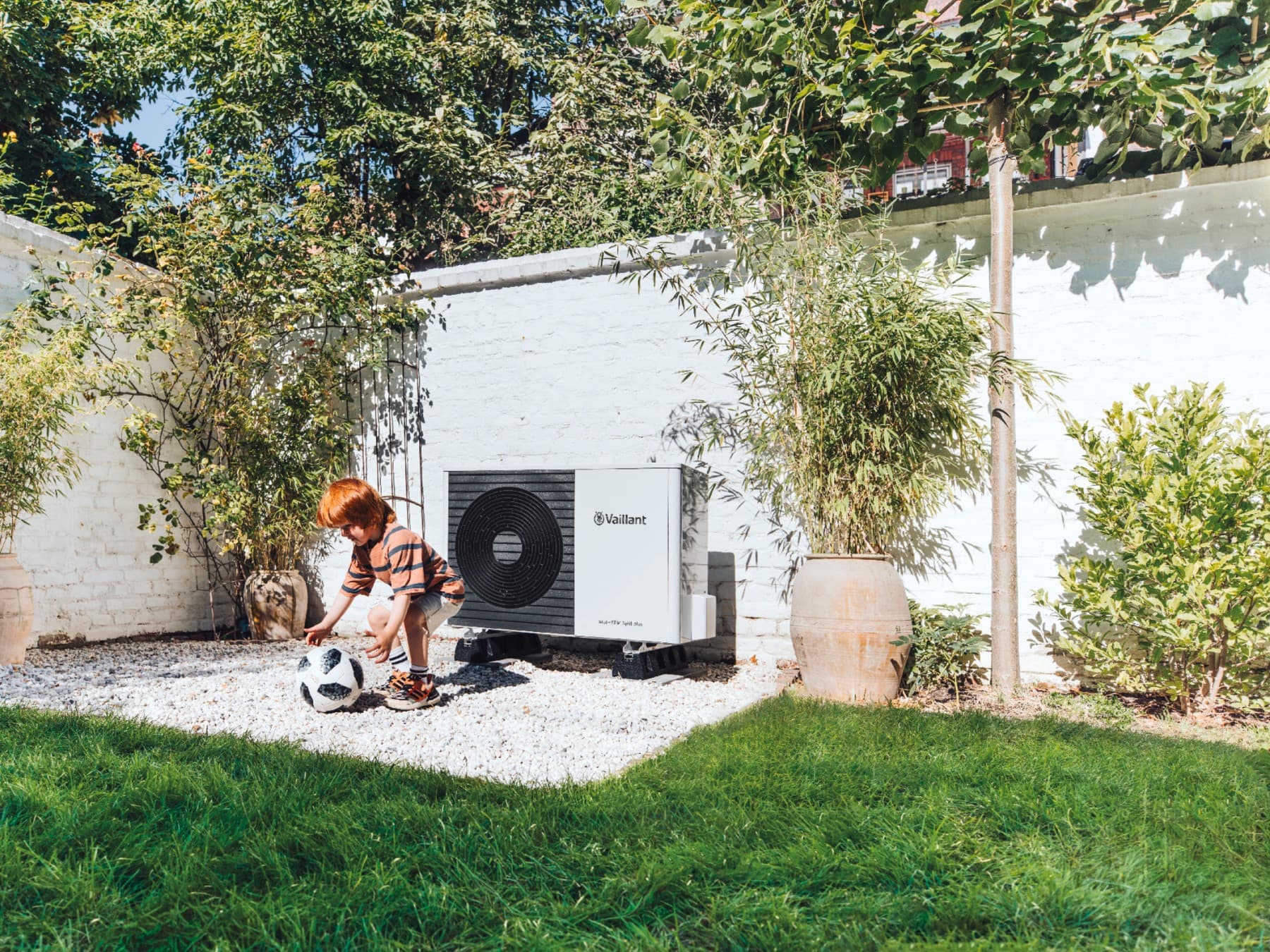 child playing with a ball in front of a heat pump in the garden