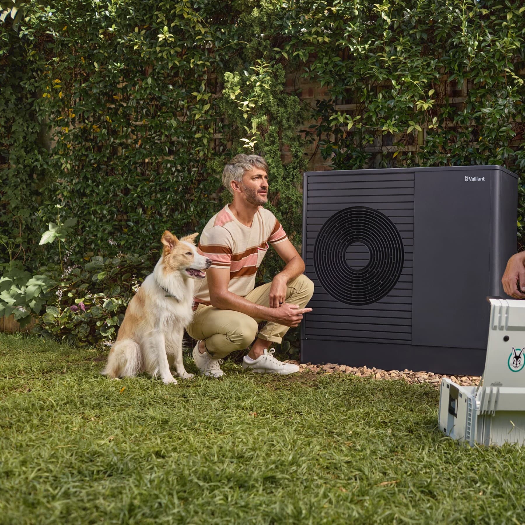 An installer is crouching in front of a heat pump and explaining something to a man.