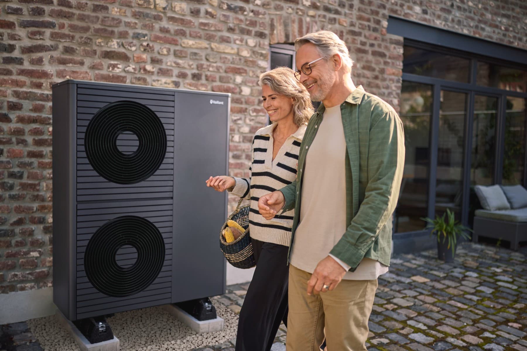 A couple walking in front of a heat pump outside their house